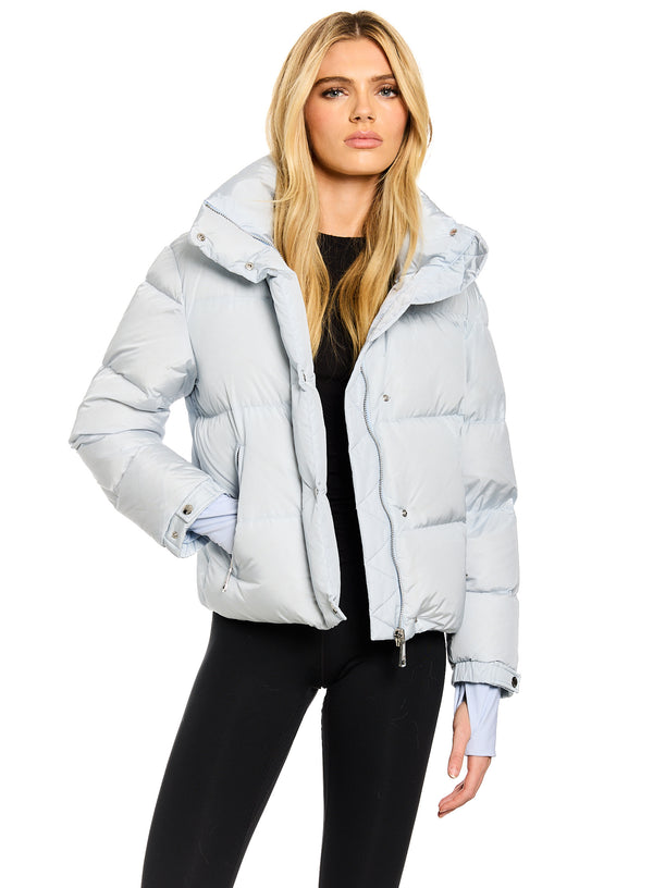 ANDI A blonde model wearing a light blue puffer jacket over a black top and black leggings, photographed against a solid white background.