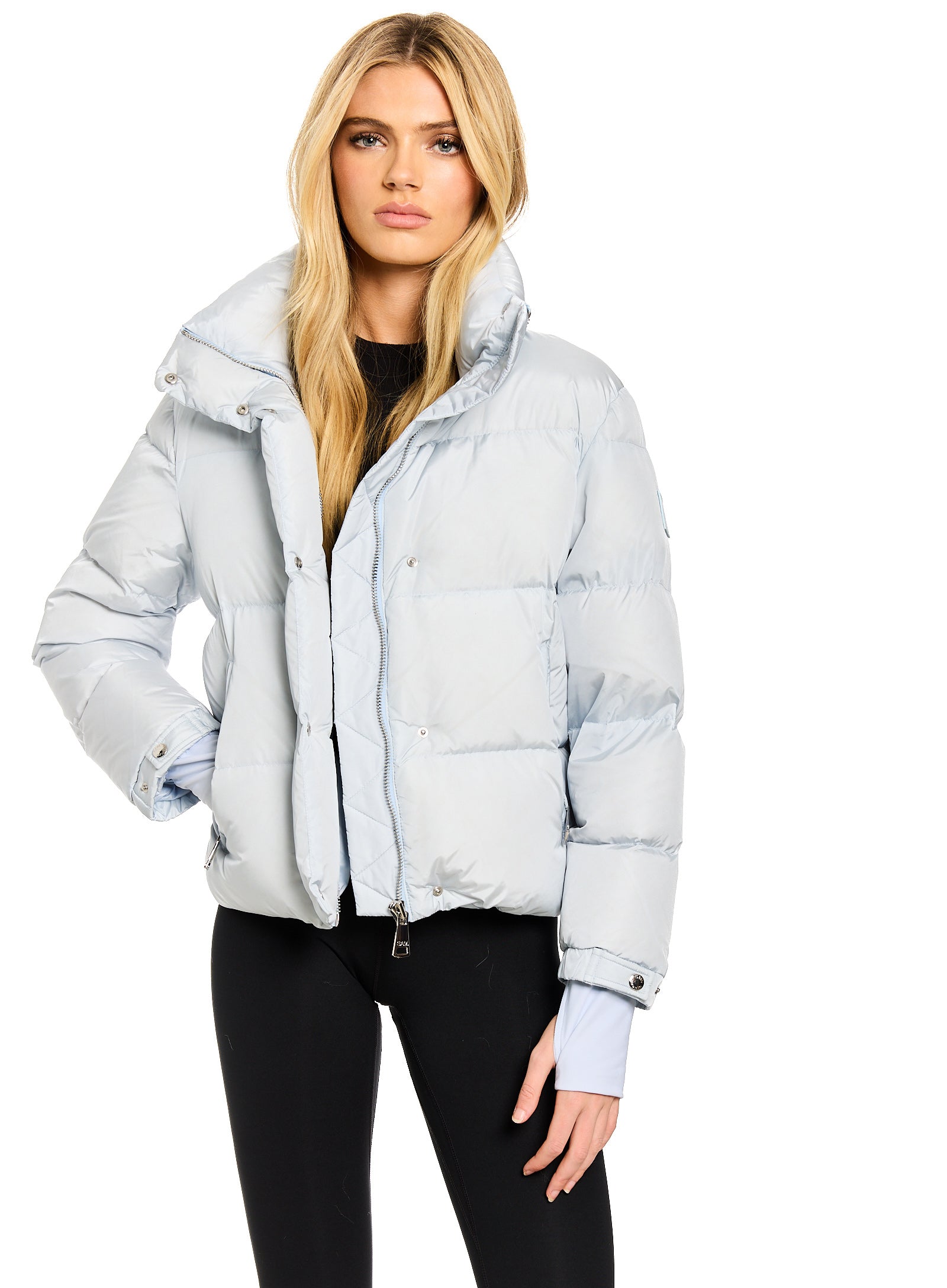 ANDI A blonde model wearing a light blue puffer jacket with a high collar, styled over a black top and black pants, against a plain white background.