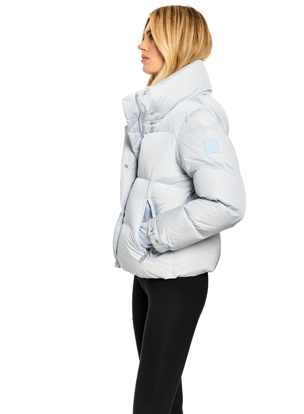 ANDI A woman shown in profile wearing a light icy blue puffer jacket with a high collar and black leggings, photographed against a solid white background.