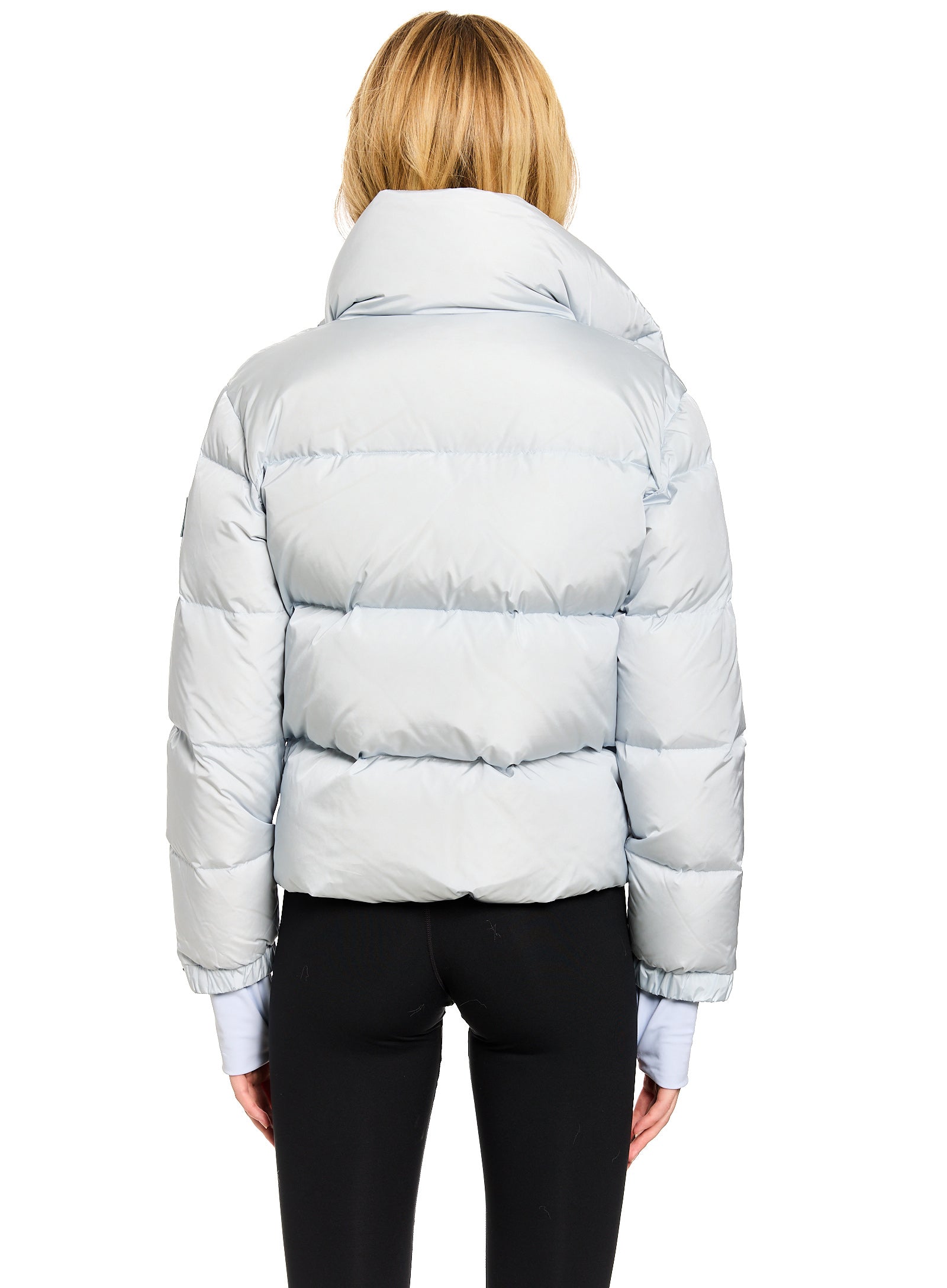 ANDI A woman viewed from the back wearing a light icy blue puffer jacket and black pants against a plain white background.