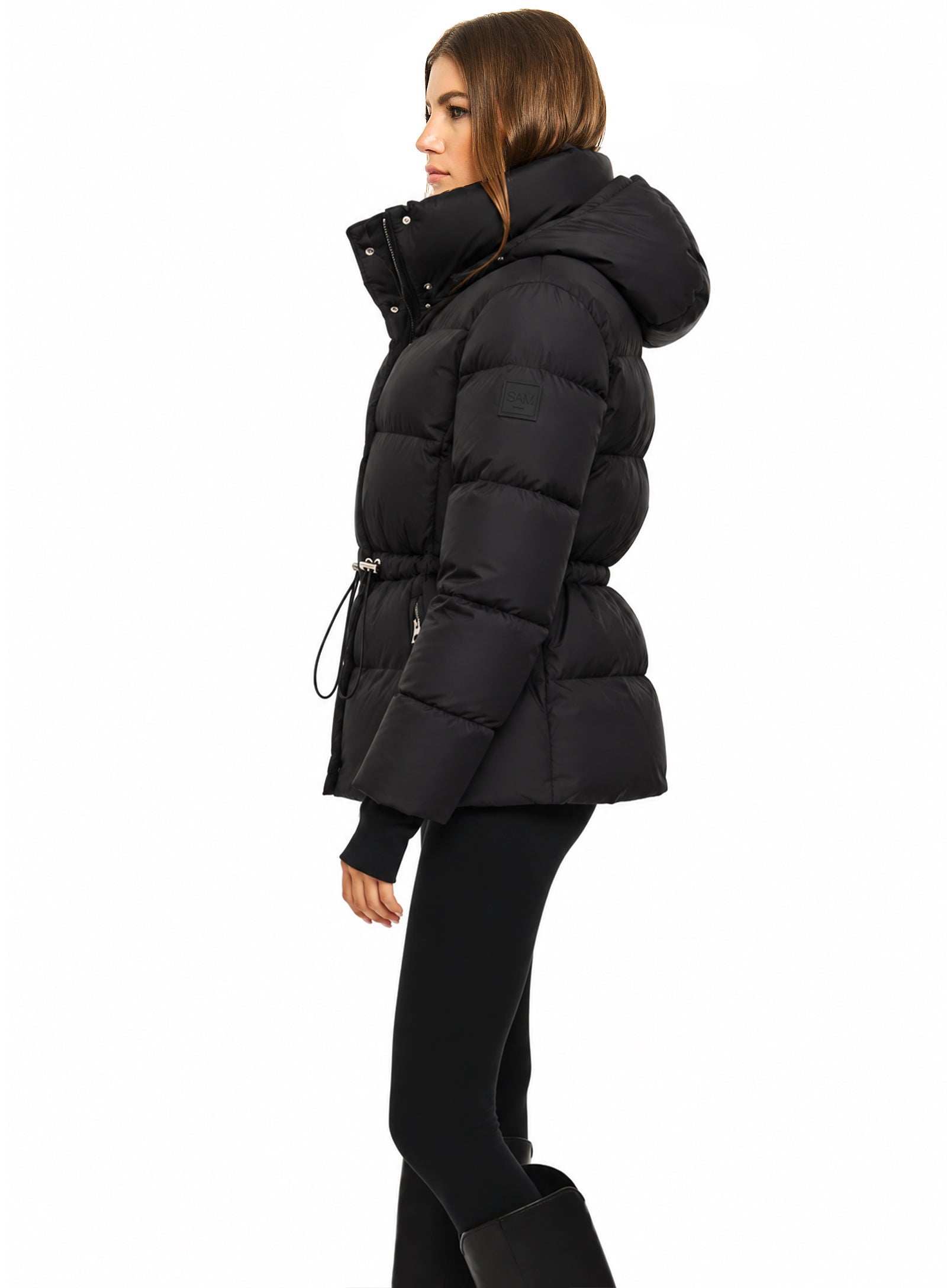 DELANEY A woman modeling a black puffer jacket with a hood, belted waist, and silver zipper details, set against a plain white background.