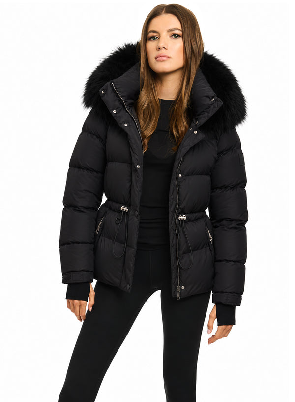 DELANEY A woman modeling a black puffer jacket with a large black fur-trimmed hood, belted waist, and silver zipper details, set against a plain white background.