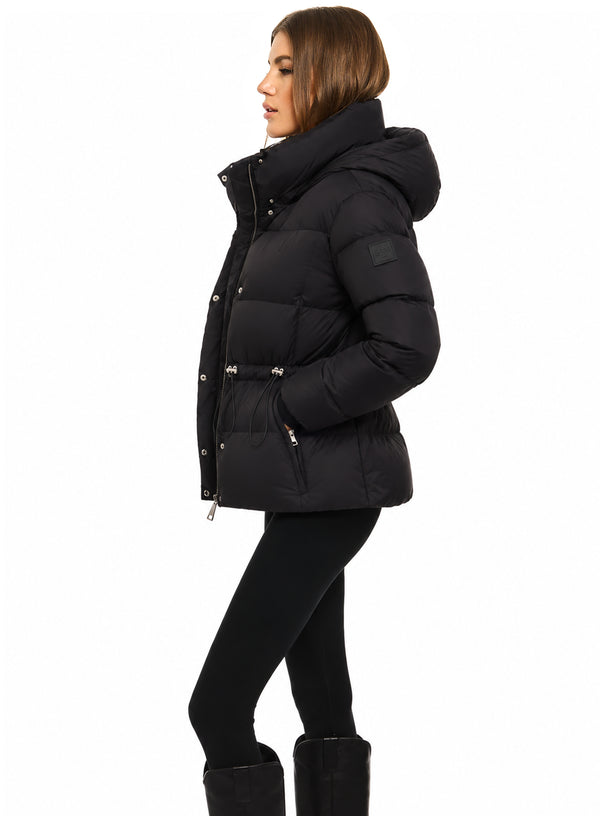 DELANEY A woman modeling a black puffer jacket with a hood, belted waist, and silver zipper details, set against a plain white background.