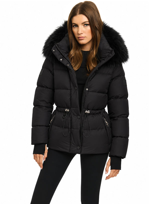DELANEY A woman modeling a black puffer jacket with a large black fur-trimmed hood, belted waist, and silver zipper details, set against a plain white background.